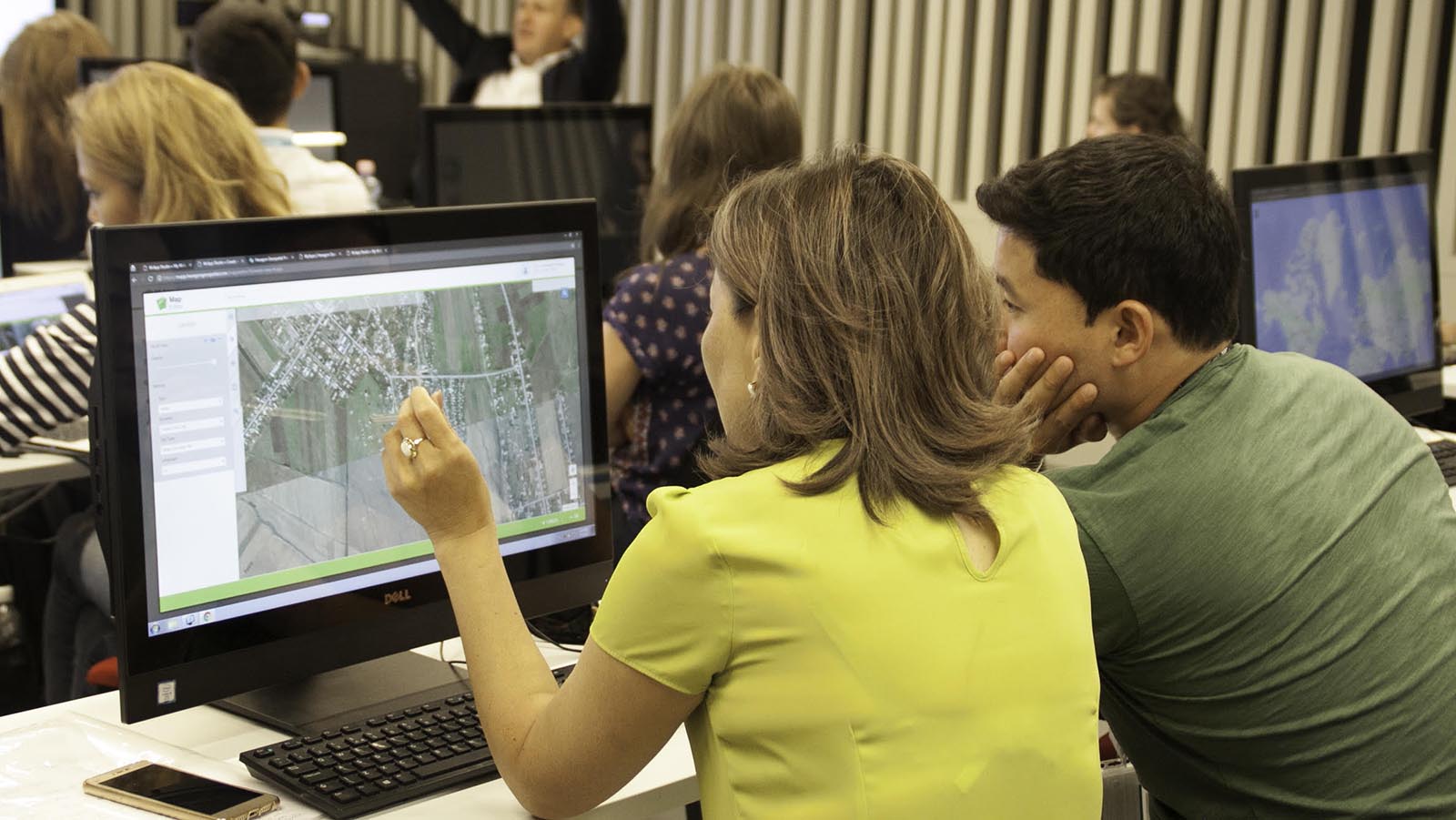 Two people behind a computer screen looking at maps